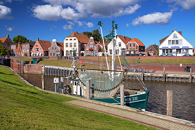 Deutschland, Niedersachsen, Nordseeküste,Ostfriesland, Fischkutter im Hafen mit historischen Backsteinhäusern im Hintergrund